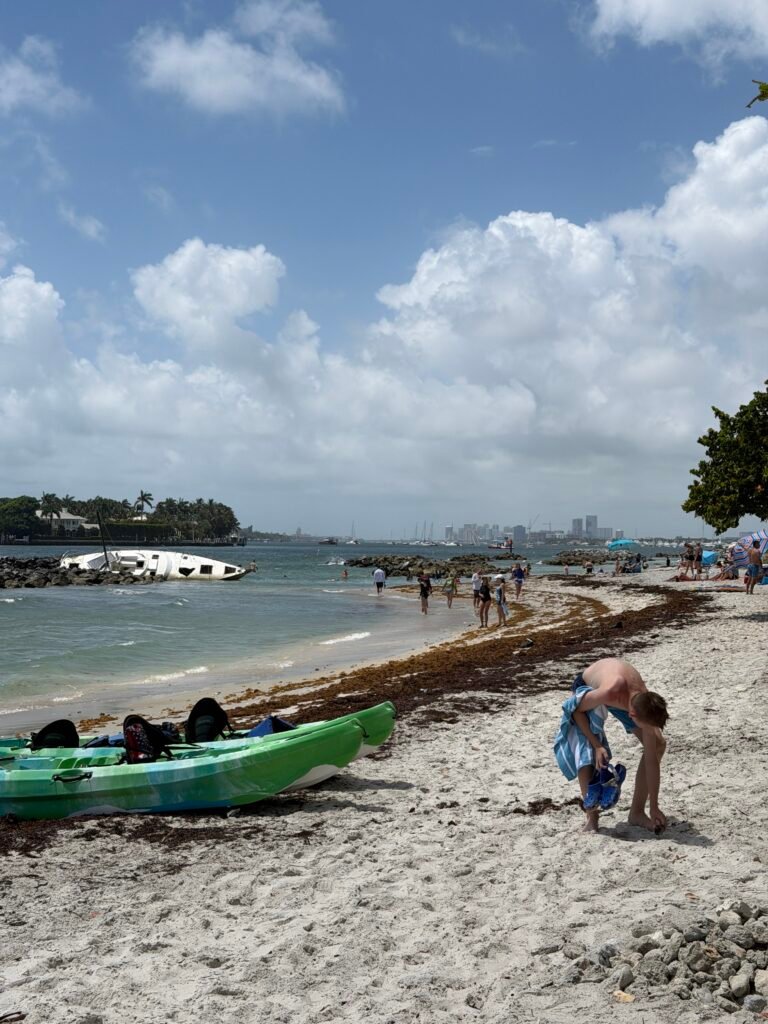 Kayaks on a Peanut Island beach near the rock breakwaters, with the West Palm Beach skyline in the distance