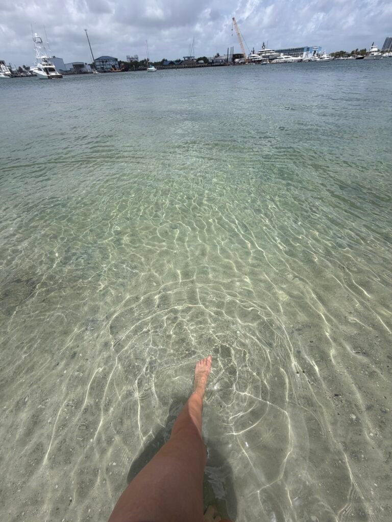 Clear, shallow water over sand at Peanut Island, with boats and the Riviera Beach marina in the background