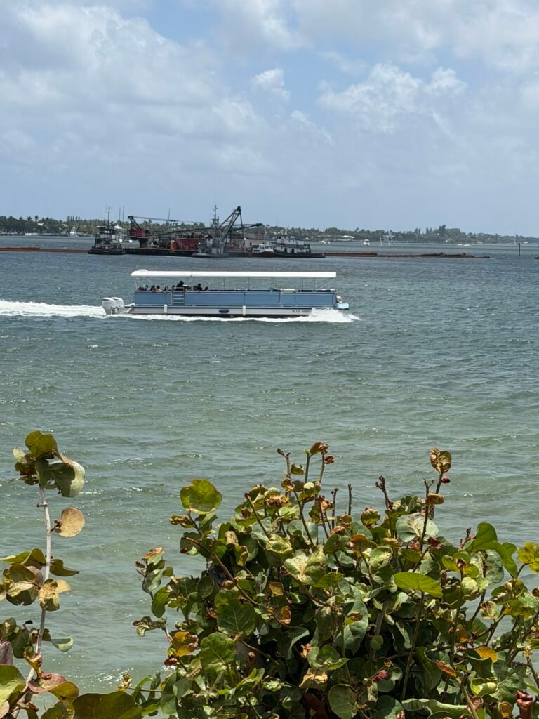 Peanut Island shuttle boat crossing the Lake Worth Lagoon, with a dredging barge behind it
