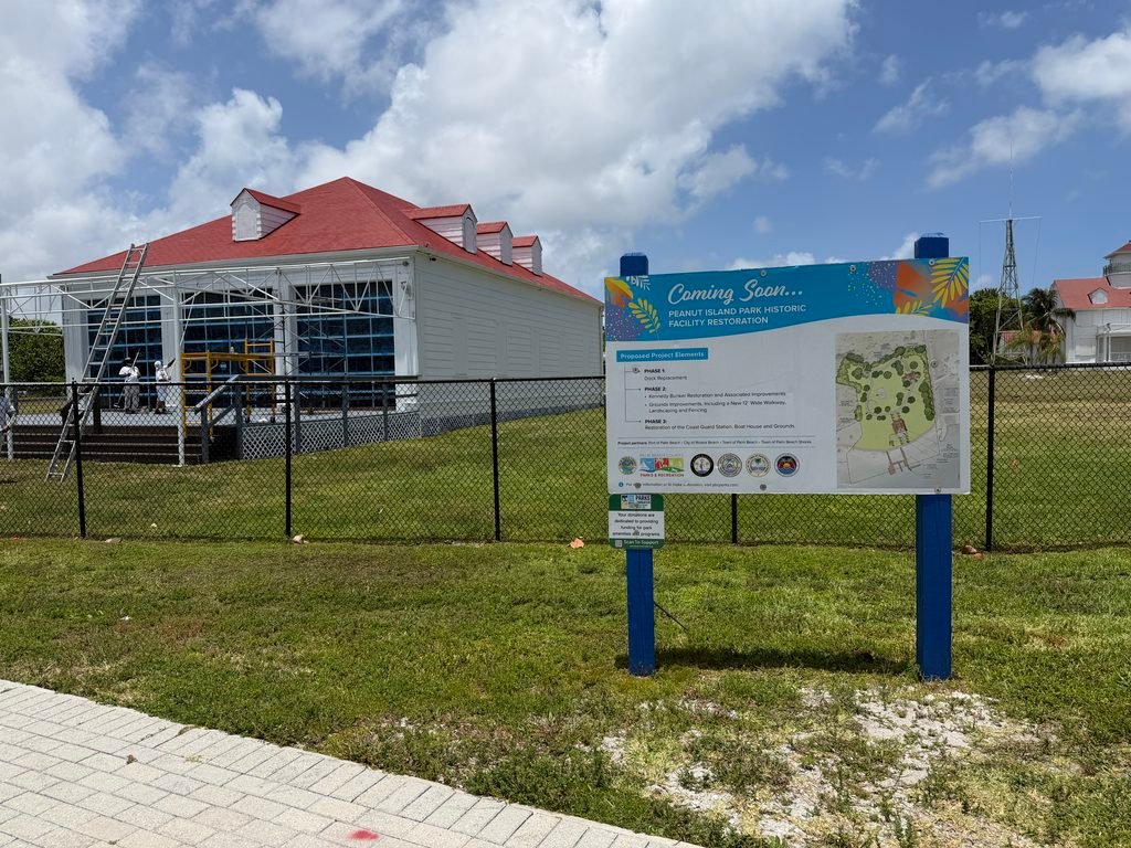 Historic Coast Guard boathouse under restoration on Peanut Island, next to a "Coming Soon" sign describing the project