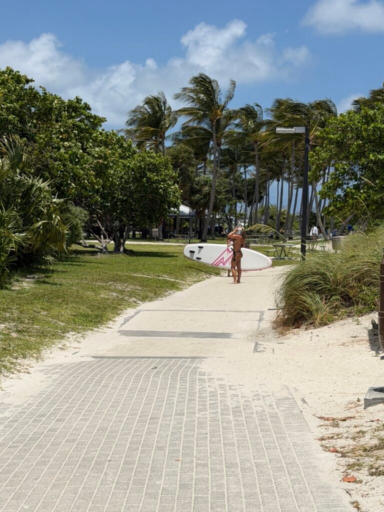 Visitor carrying a paddleboard along the paved path past the Peanut Island picnic area